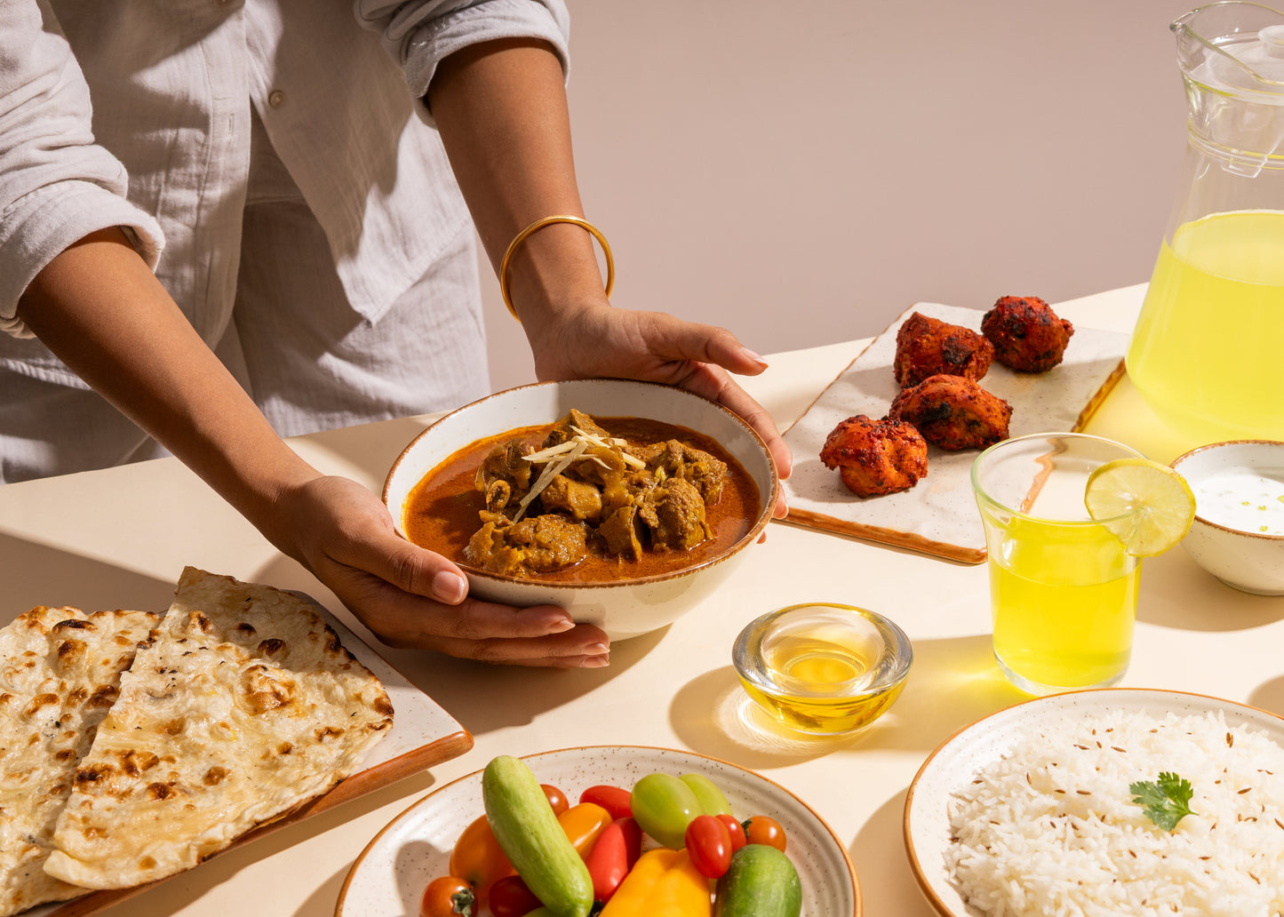 Person holding a bowl of curry with a table full of food including rice, naan, and vegetables.