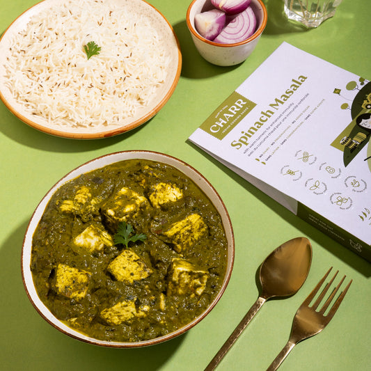 Bowl of spinach masala with rice, onions, and a recipe book on a green table.