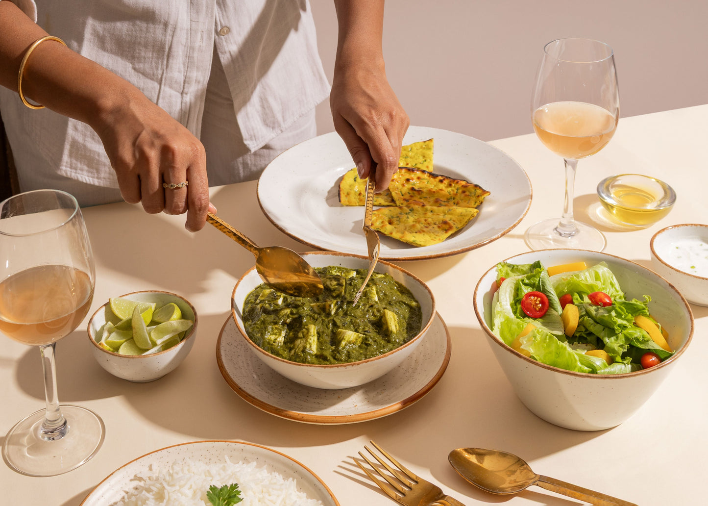 Dining table with a meal including a bowl of green curry, salad, and wine glasses.
